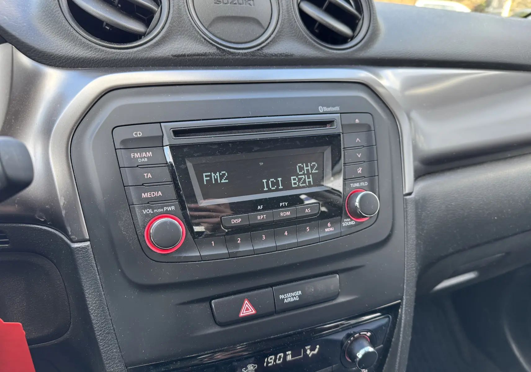Gros plan sur la console centrale noire du Suzuki Vitara blanc 2023, avec radio affichant FM2 et boutons rouges.