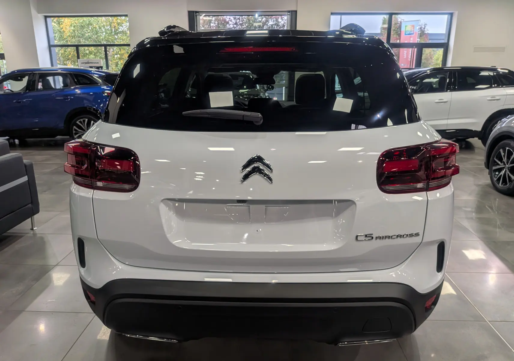 Vue arrière d'un Citroën C5 Aircross hybride blanc Okénite avec toit noir, en showroom lumineux.