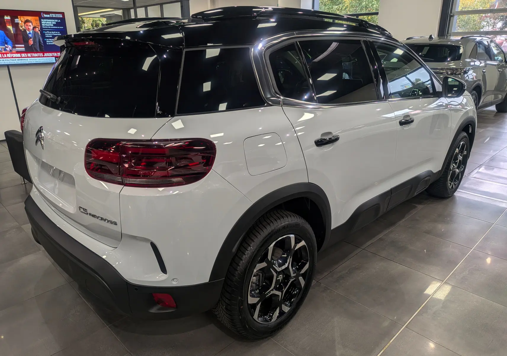 Vue 3/4 arrière droite du Citroën C5 Aircross hybride blanc Okénite avec toit noir et jantes biton dans un showroom.