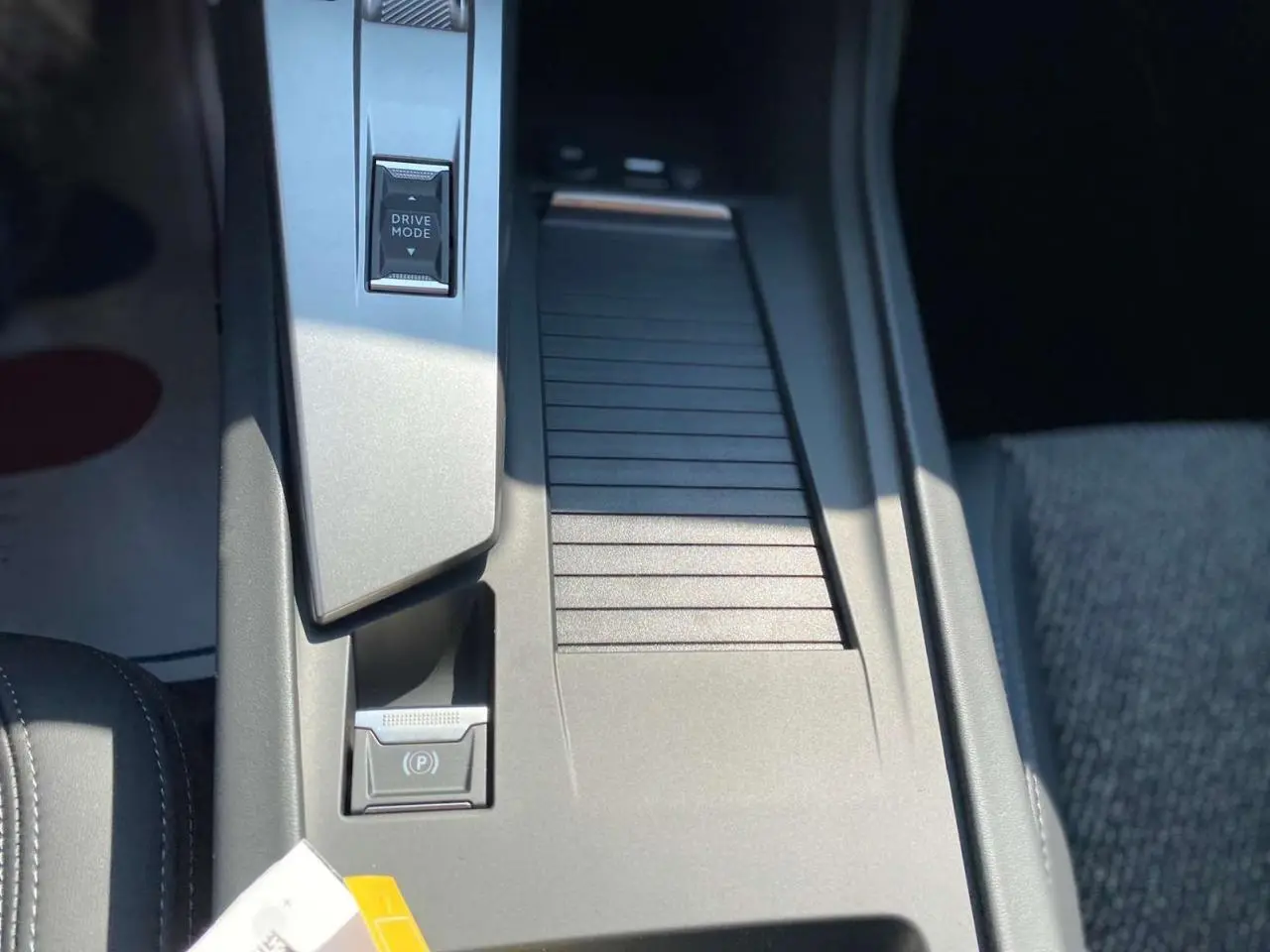Gros plan sur la console centrale de la Peugeot 308 GT 2025 gris selenium, avec bouton Drive Mode et frein à main électrique.