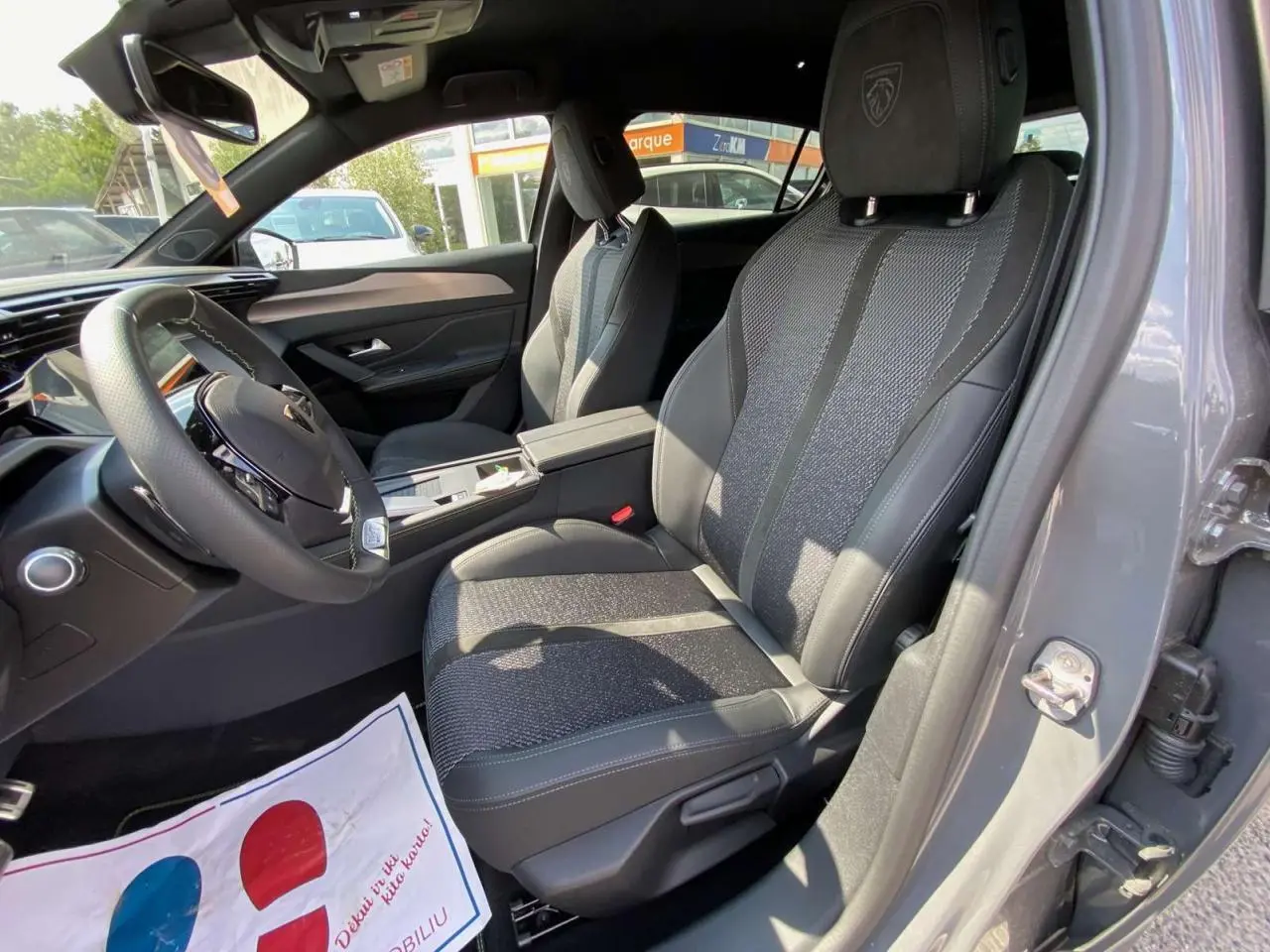 Intérieur avant droit de la Peugeot 308 GT 2025 gris selenium, sièges en tissu et cuir avec logo Peugeot brodé sur l'appui-tête.