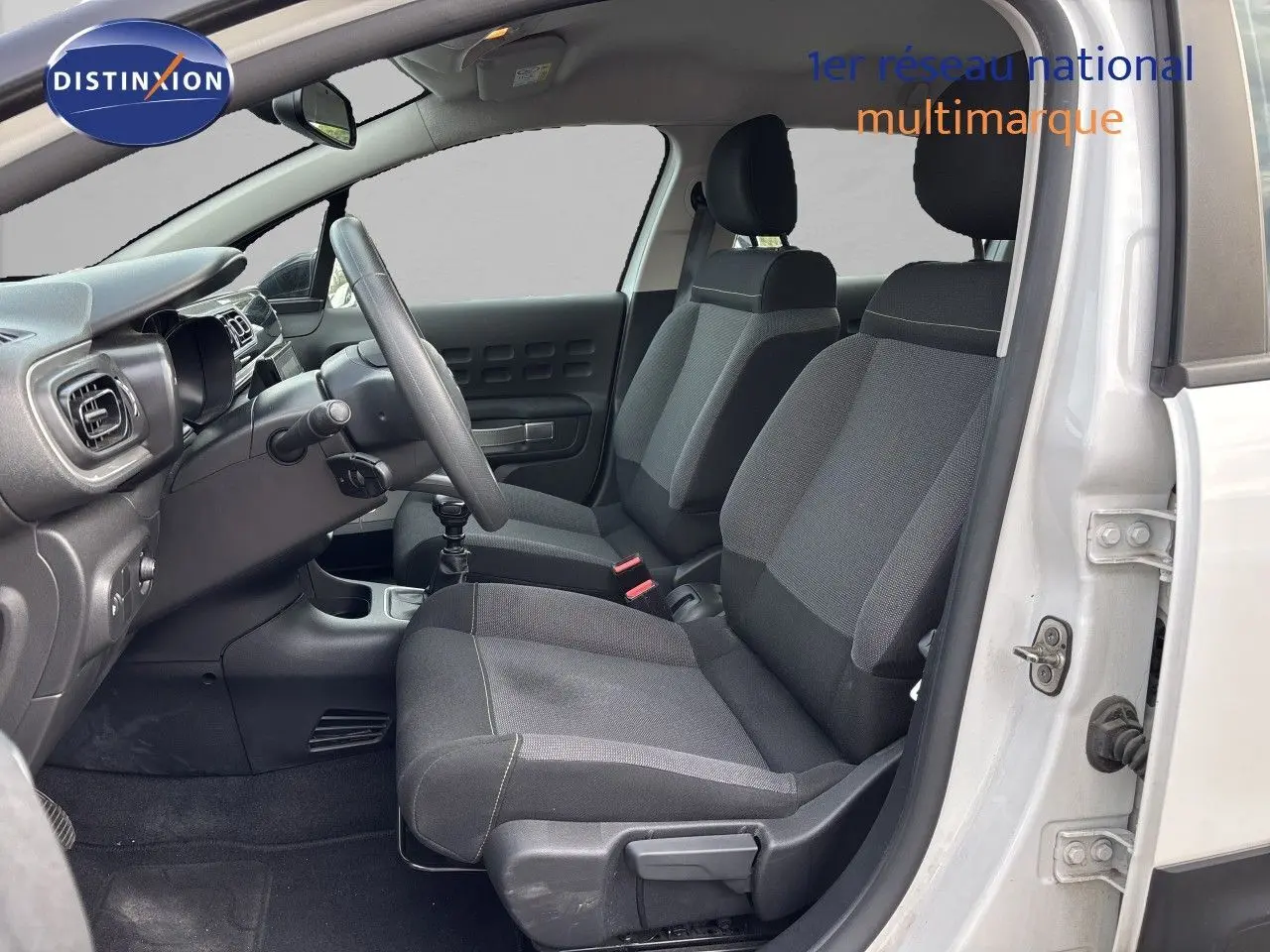 Vue intérieure côté conducteur de la Citroën C3 blanche banquise 2022, sièges tissu gris et tableau de bord noir.
