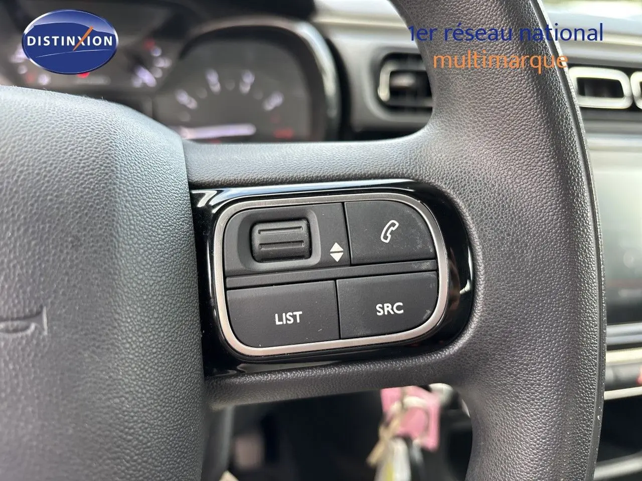 Gros plan sur les commandes gauche du volant noir de la Citroën C3 blanche, avec boutons de gestion audio et appel.