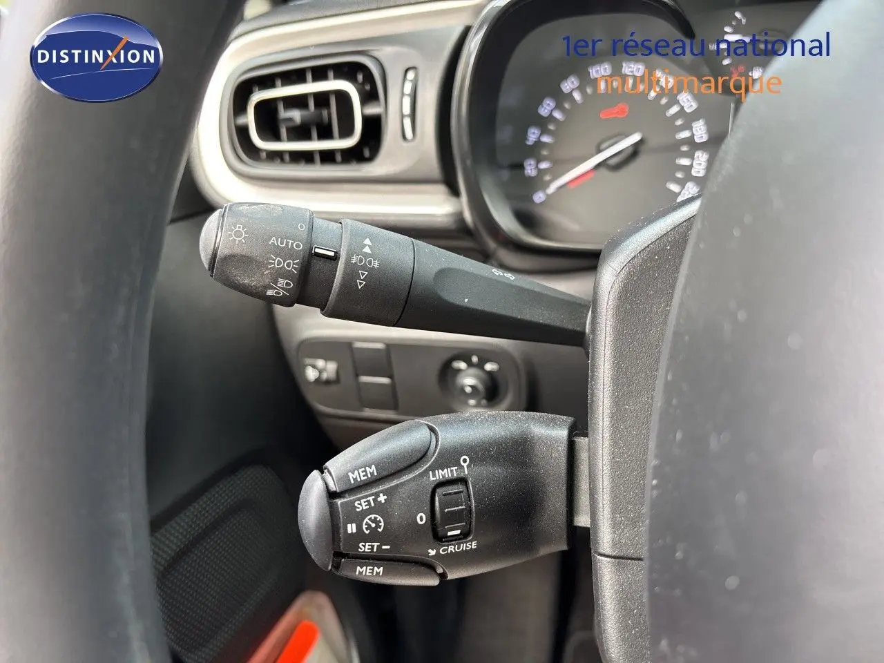Gros plan sur les commandes au volant côté gauche de la Citroën C3 blanche, avec tableau de bord et aérateur visibles.