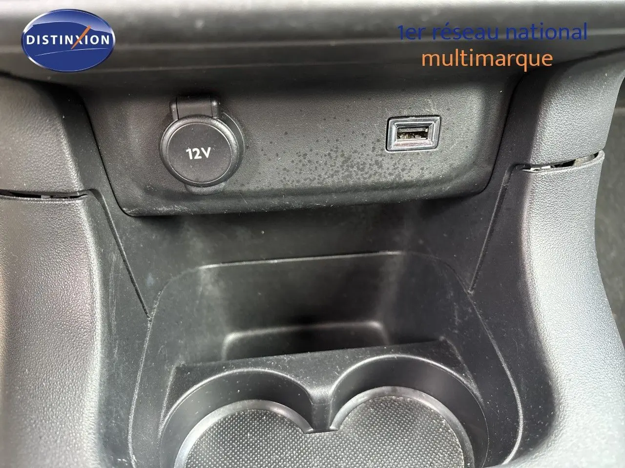 Gros plan sur la console centrale d’une Citroën C3 blanche, montrant prise 12V et port USB au-dessus des porte-gobelets.