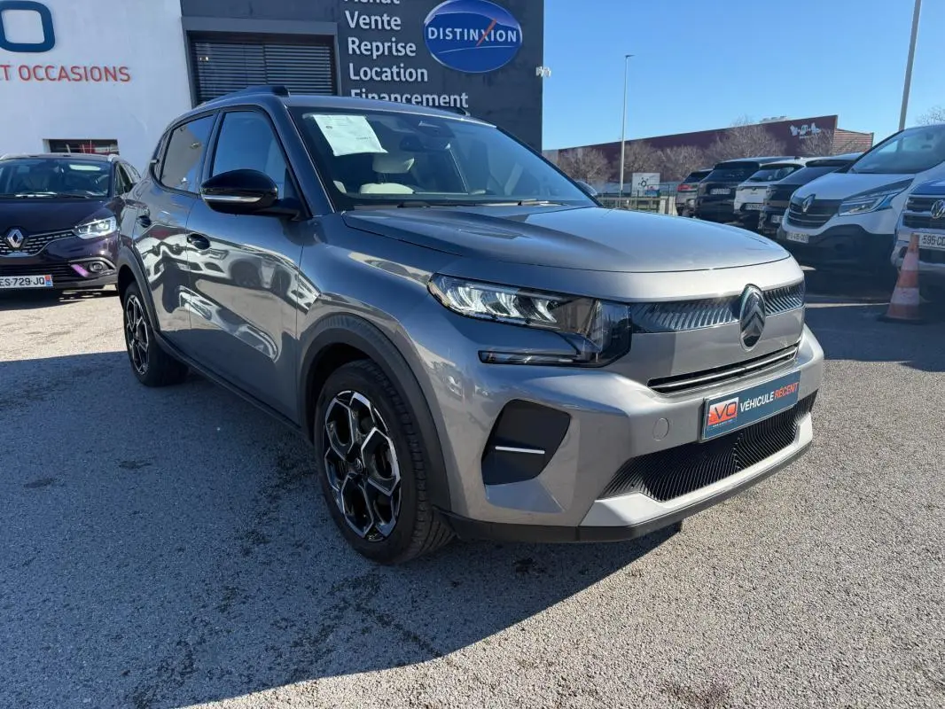 Vue 3/4 avant droite d'une Citroën C3 gris métallisé 2025 avec jantes alliage 17 pouces et barres de toit.