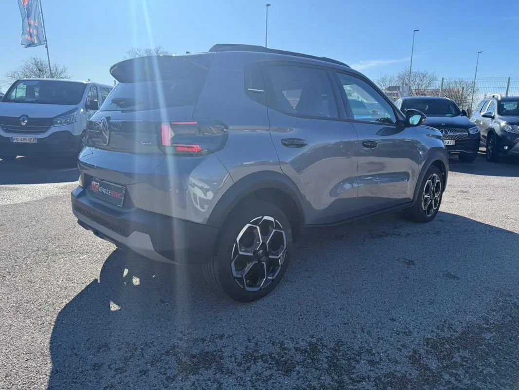 Citroën C3 gris vue 3/4 arrière droit, avec barres de toit et jantes alliage 17 pouces sous un ciel bleu.