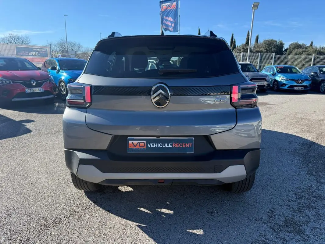 Vue arrière d'une Citroën C3 gris 2025 avec feux arrière LED et barres de toit visibles sur parking.