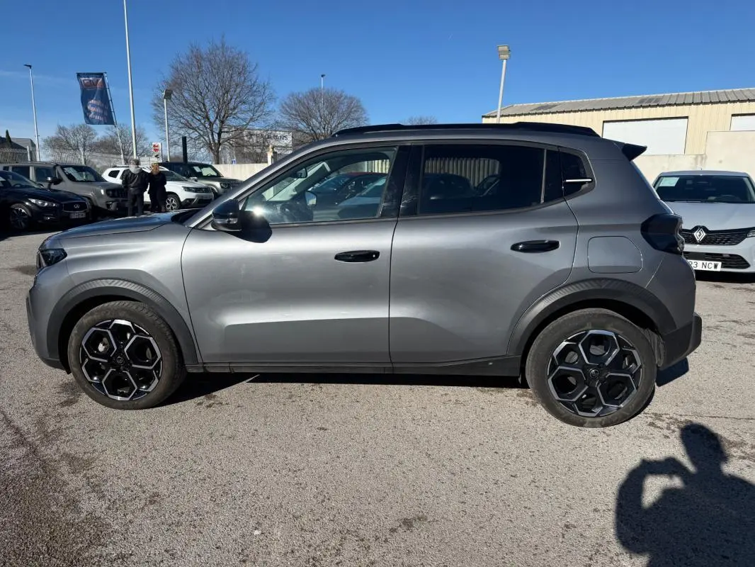 Vue de profil côté gauche d'une Citroën C3 gris 2025 avec jantes alliage noires et barres de toit visibles.