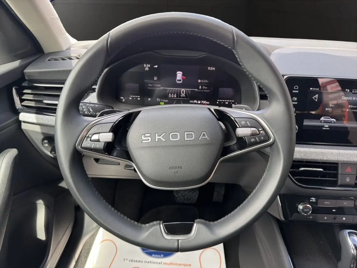 Vue intérieure centrée sur le volant SKODA gris foncé avec tableau de bord numérique et écran tactile central.