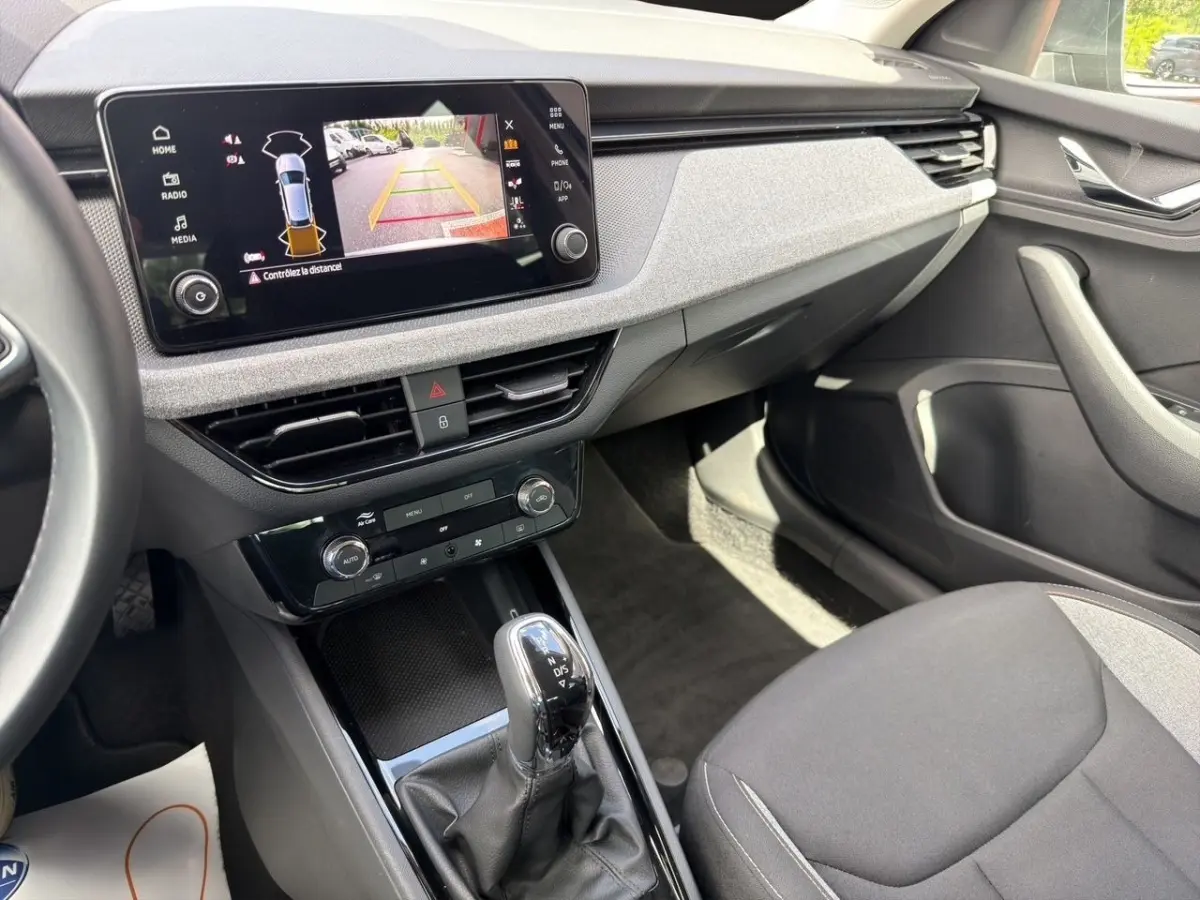 Vue intérieure côté passager de la Skoda Scala gris foncé, avec écran tactile affichant la caméra de recul et levier de boîte auto.