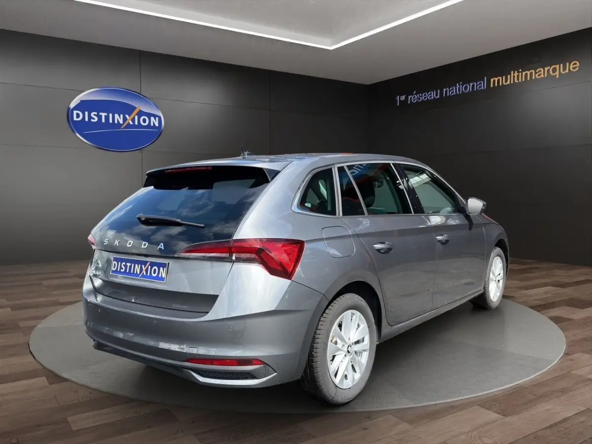 Vue 3/4 arrière droite d'une Skoda Scala gris foncé exposée en showroom avec feux arrière LED et jantes blanches.