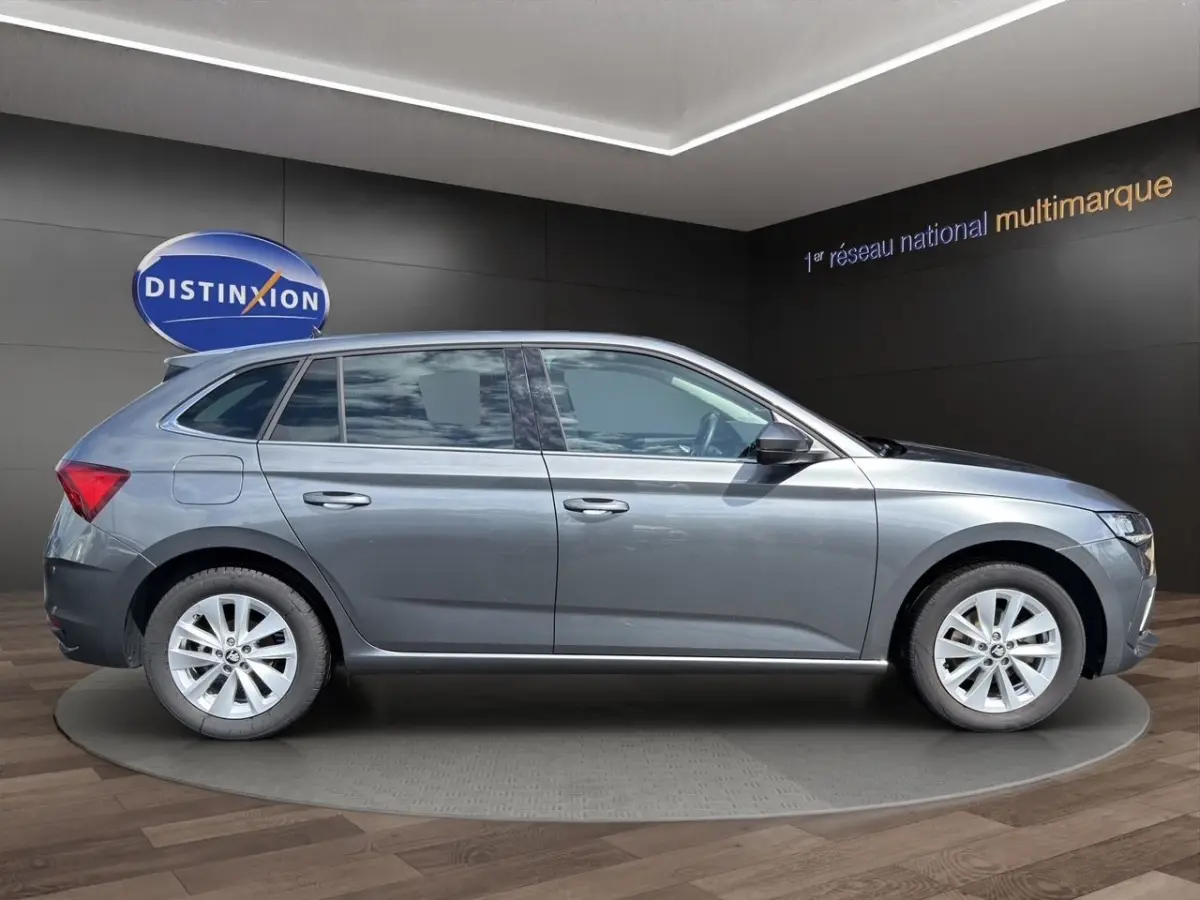 Vue de profil côté gauche d'une SKODA SCALA gris foncé 2025 dans un showroom avec jantes alliage et vitres teintées.