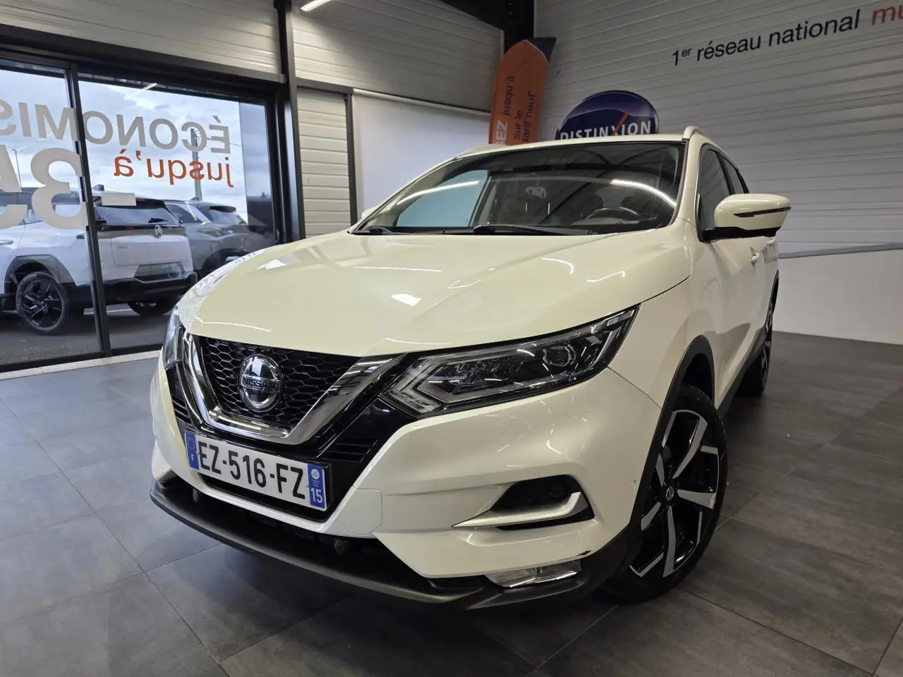 Nissan Qashqai blanc vue 3/4 avant droit en intérieur, avec jantes alliage noires et calandre chromée.