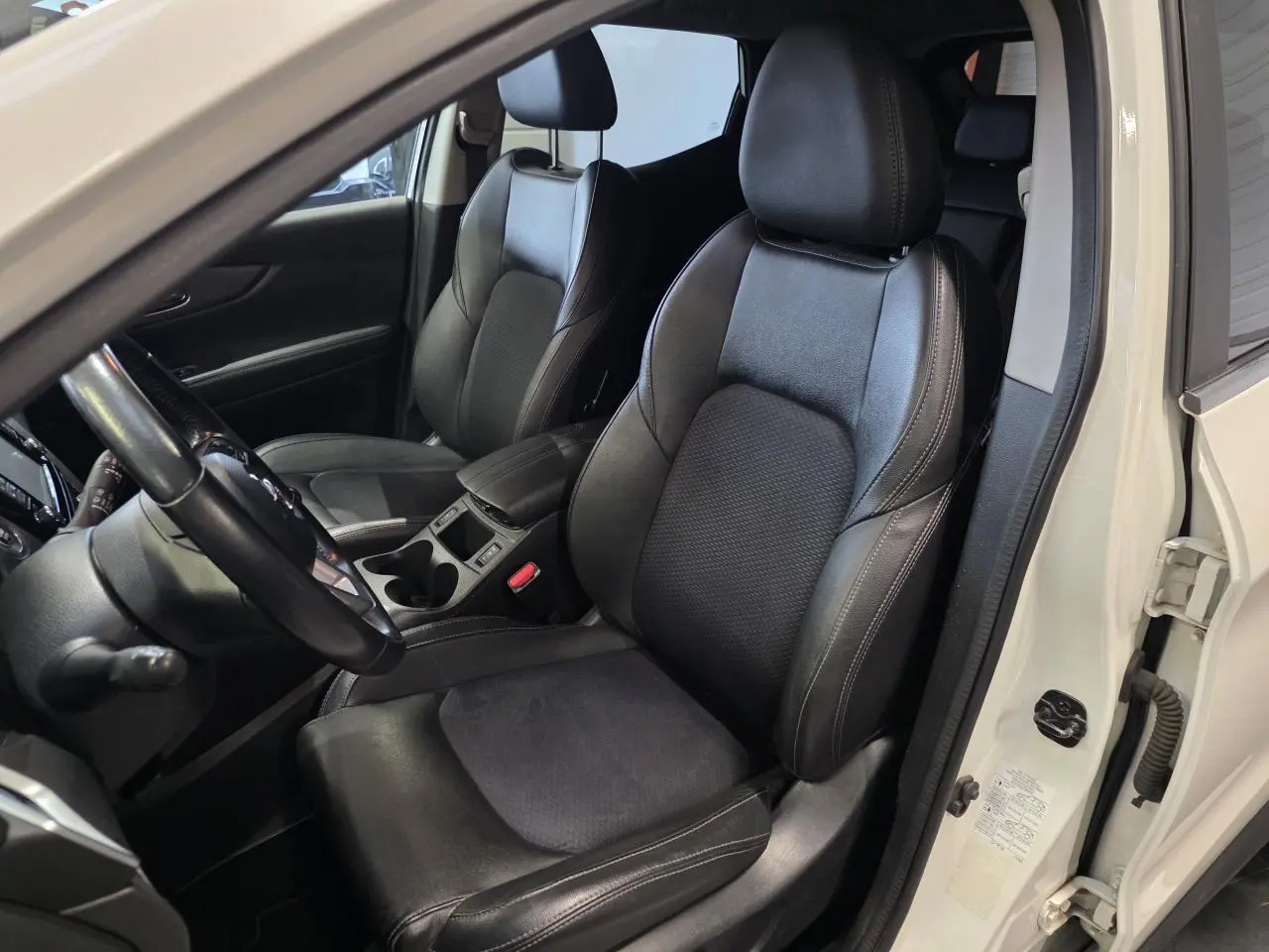 Vue intérieure côté conducteur du Nissan Qashqai blanc de 2018, sièges sport en cuir noir et accoudoir central.
