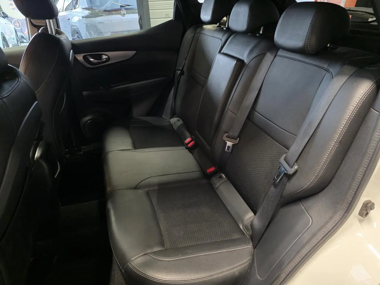 Vue intérieure côté droit des sièges arrière en cuir noir du Nissan Qashqai blanc, avec ceintures de sécurité visibles.
