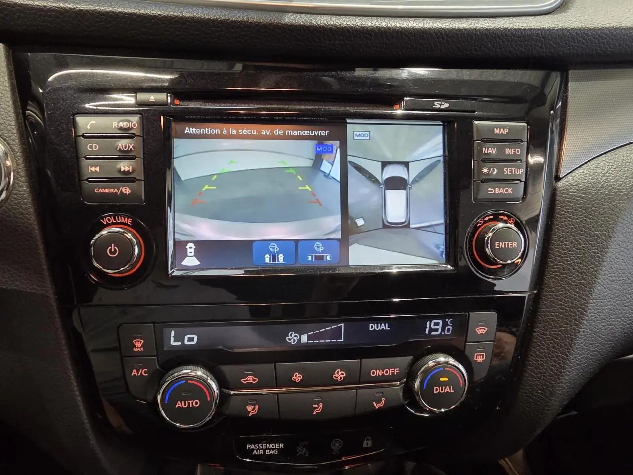 Vue rapprochée de la console centrale noire du Nissan Qashqai blanc avec écran de caméra 360° et commandes climatisation.