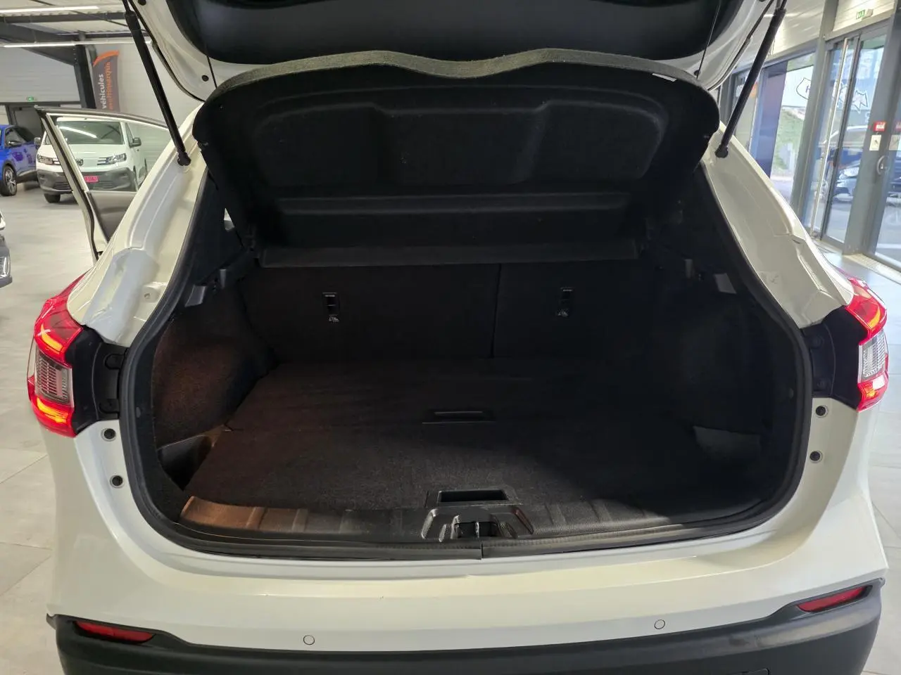 Coffre ouvert vu de l'arrière d'un Nissan Qashqai blanc avec feux arrière LED allumés en intérieur showroom.