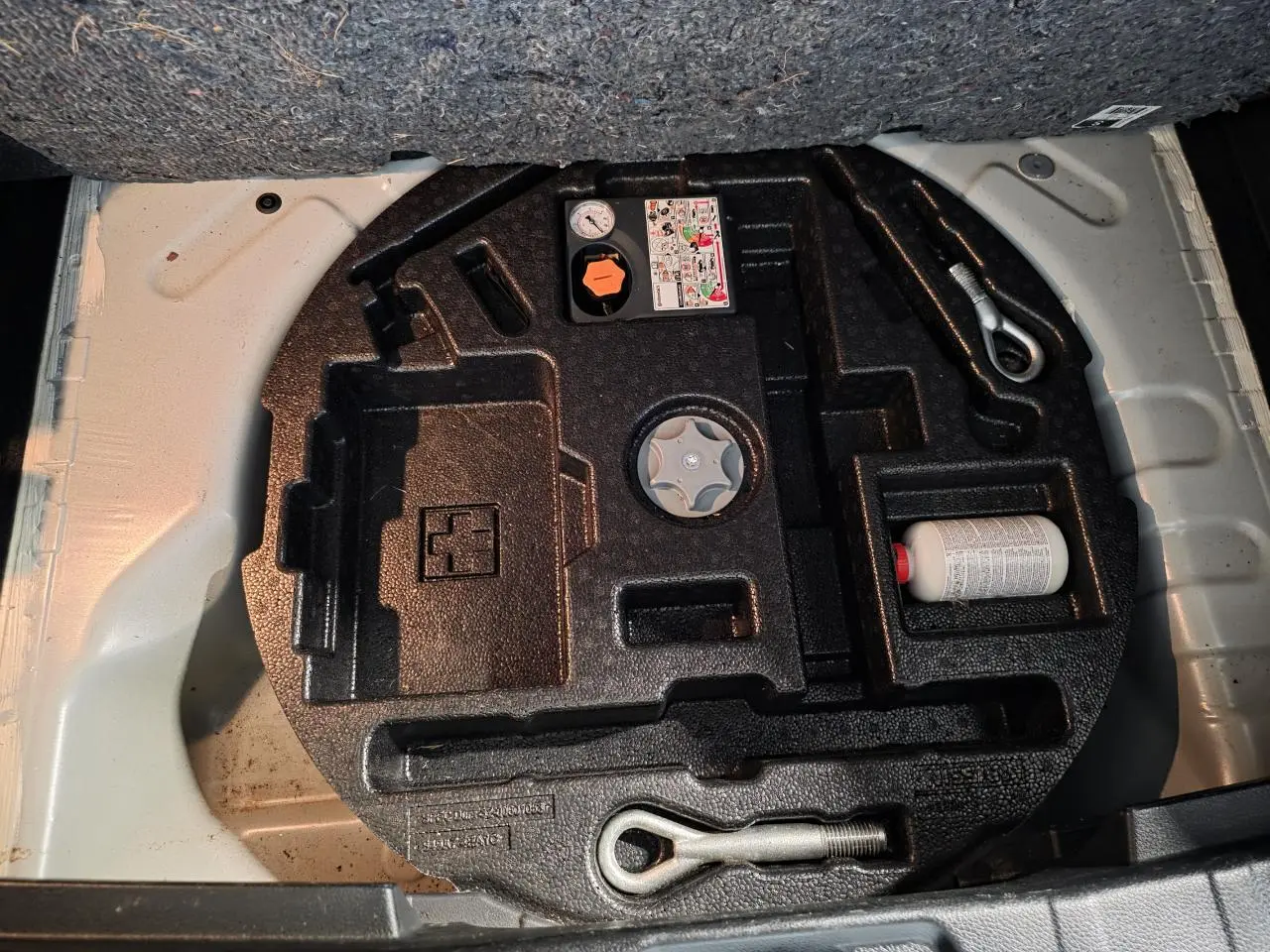 Vue du coffre ouvert montrant le kit de réparation pneumatique dans un Nissan Qashqai blanc 2018.