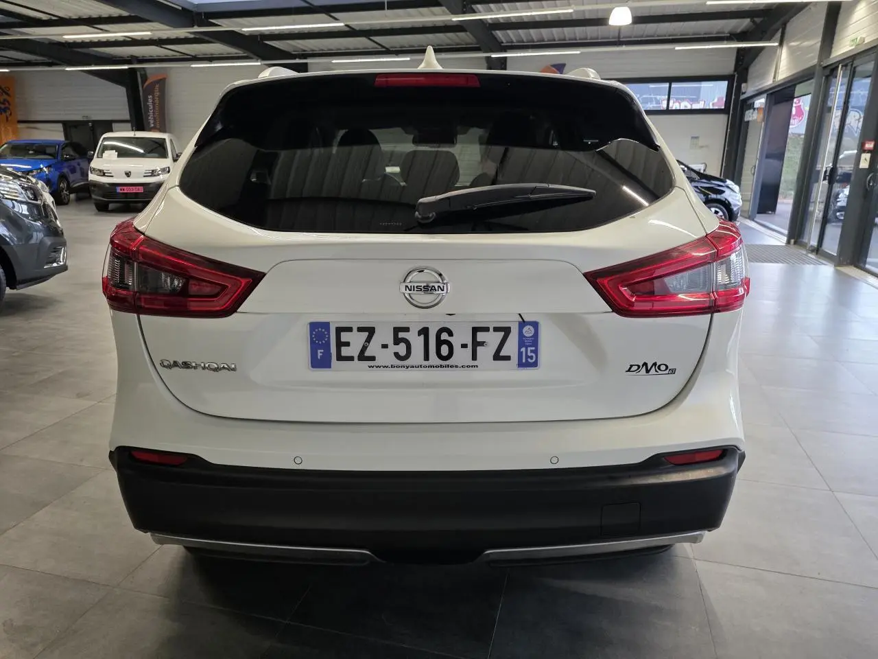 Vue arrière d'un Nissan Qashqai blanc avec feux LED et pare-chocs noir dans un showroom.