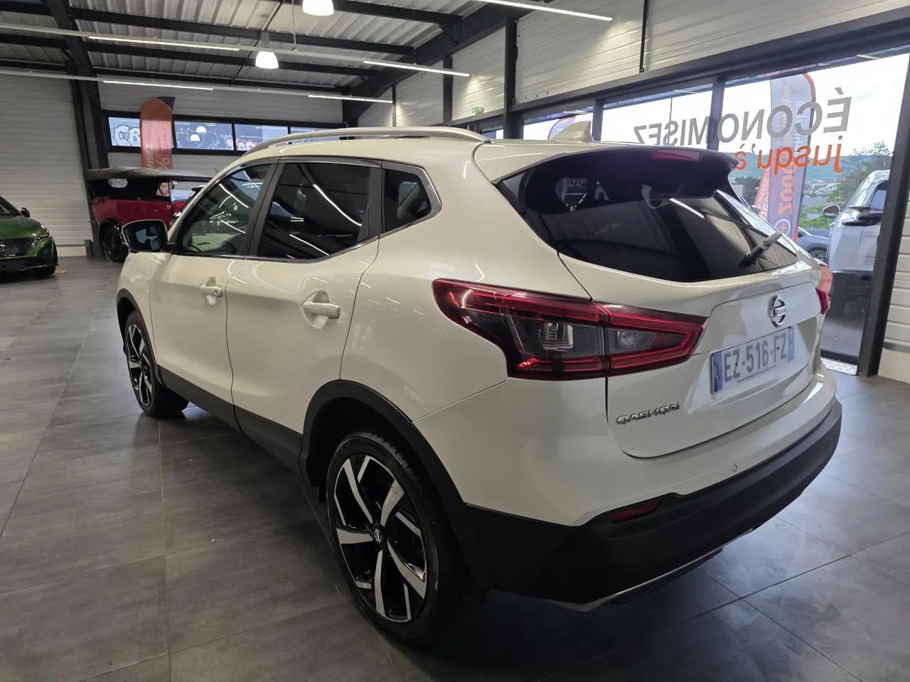 Nissan Qashqai blanc vue 3/4 arrière droit en intérieur avec jantes alliage noires et toit panoramique.