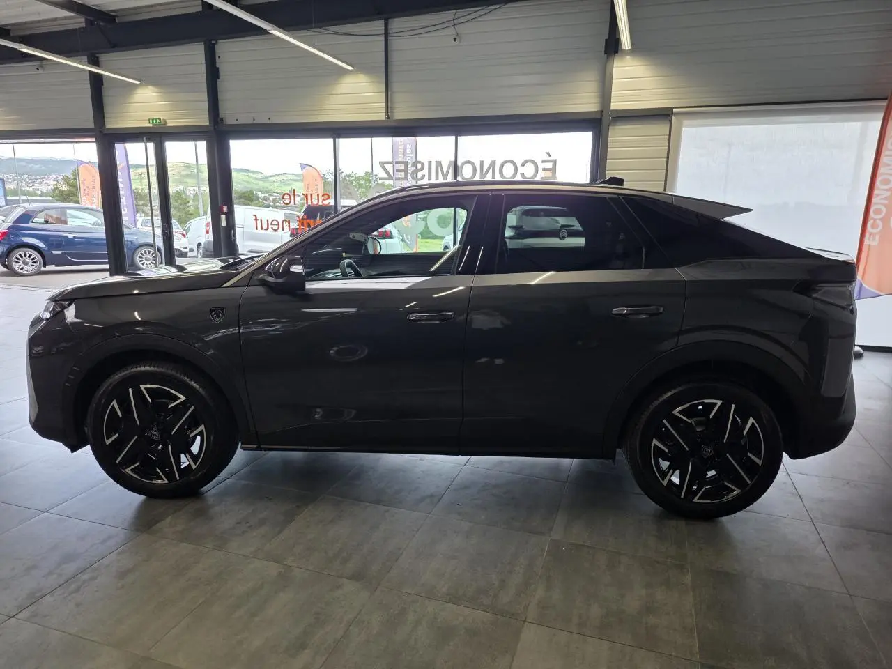 Vue de profil côté gauche d’un Peugeot 3008 gris titanium 2026 en version hybride GT Exclusive, en showroom.