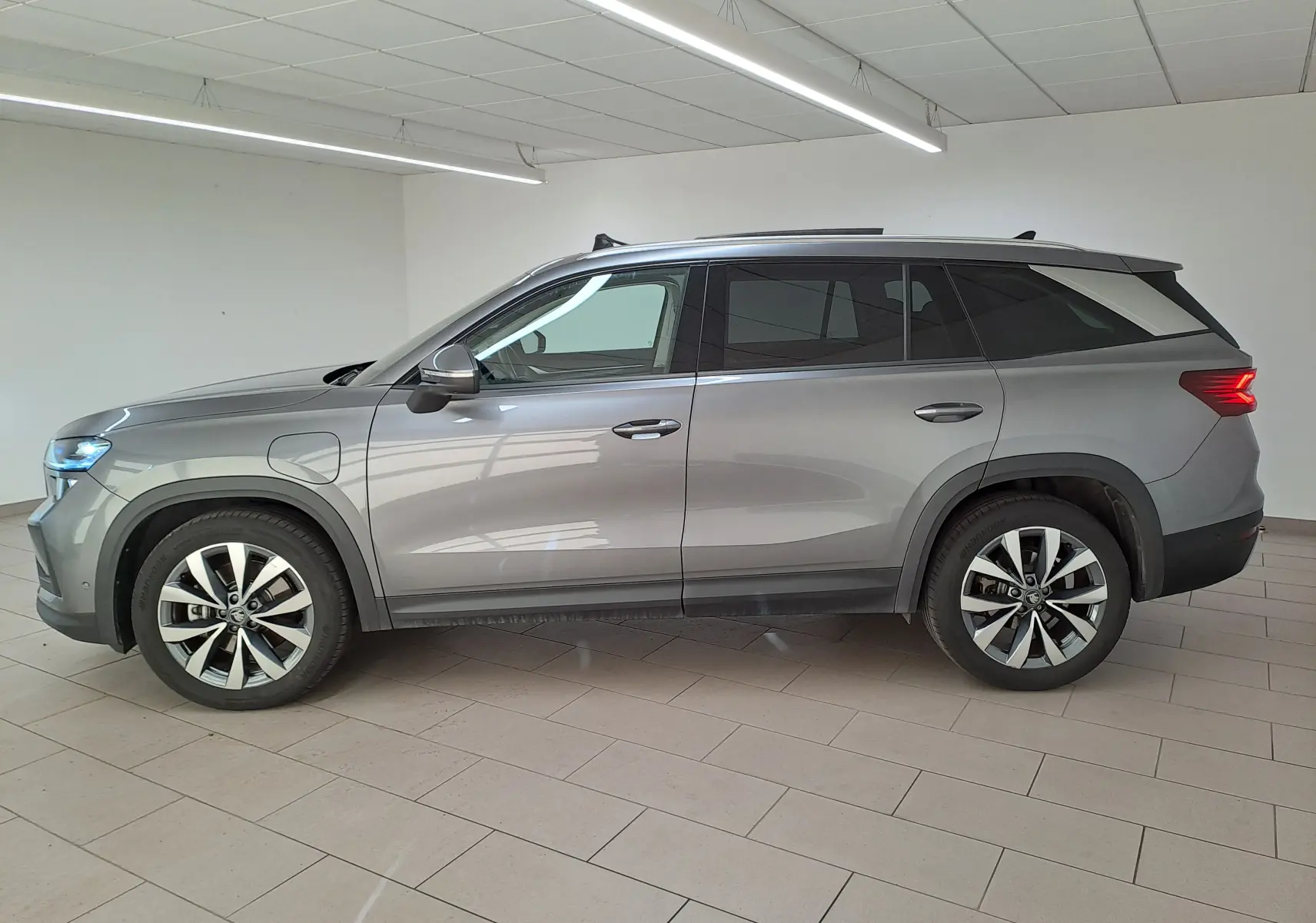 Vue de profil côté gauche d'un Skoda Kodiaq gris graphite hybride rechargeable avec jantes alliage 19 pouces dans un showroom.