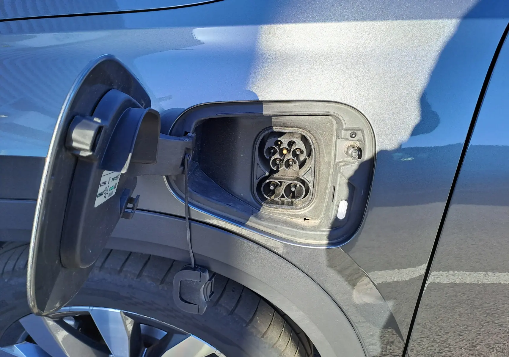 Prise de recharge ouverte côté gauche sur SUV Skoda Kodiaq gris graphite, jante alliage 19 pouces visible.