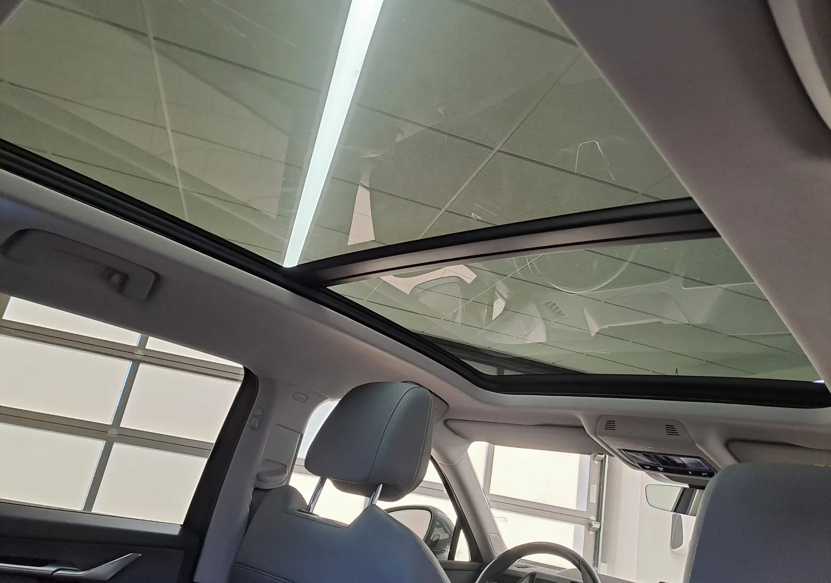 Vue intérieure du toit panoramique ouvrant en verre du Skoda Kodiaq gris graphite, avec sièges avant et tableau de bord partiellement visibles.