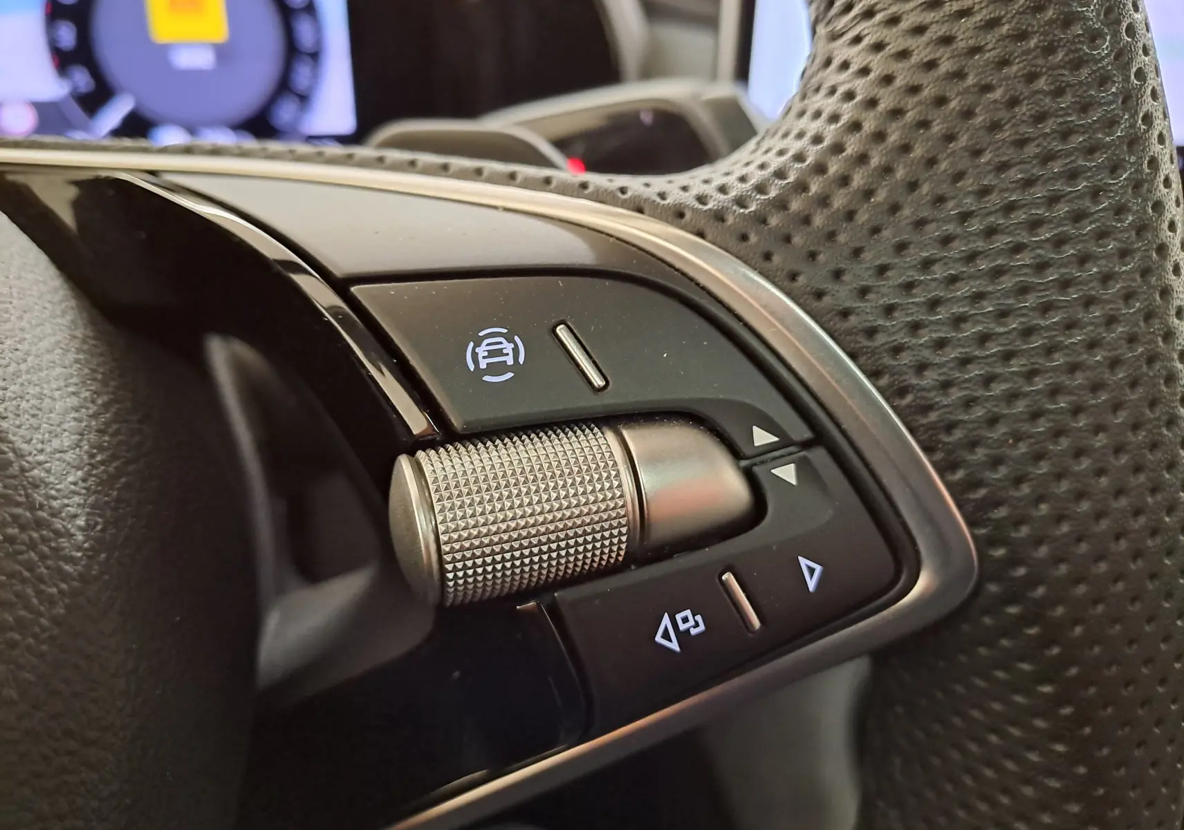 Gros plan sur les commandes du volant perforé du Skoda Kodiaq 2025, avec molette texturée et boutons rétroéclairés.