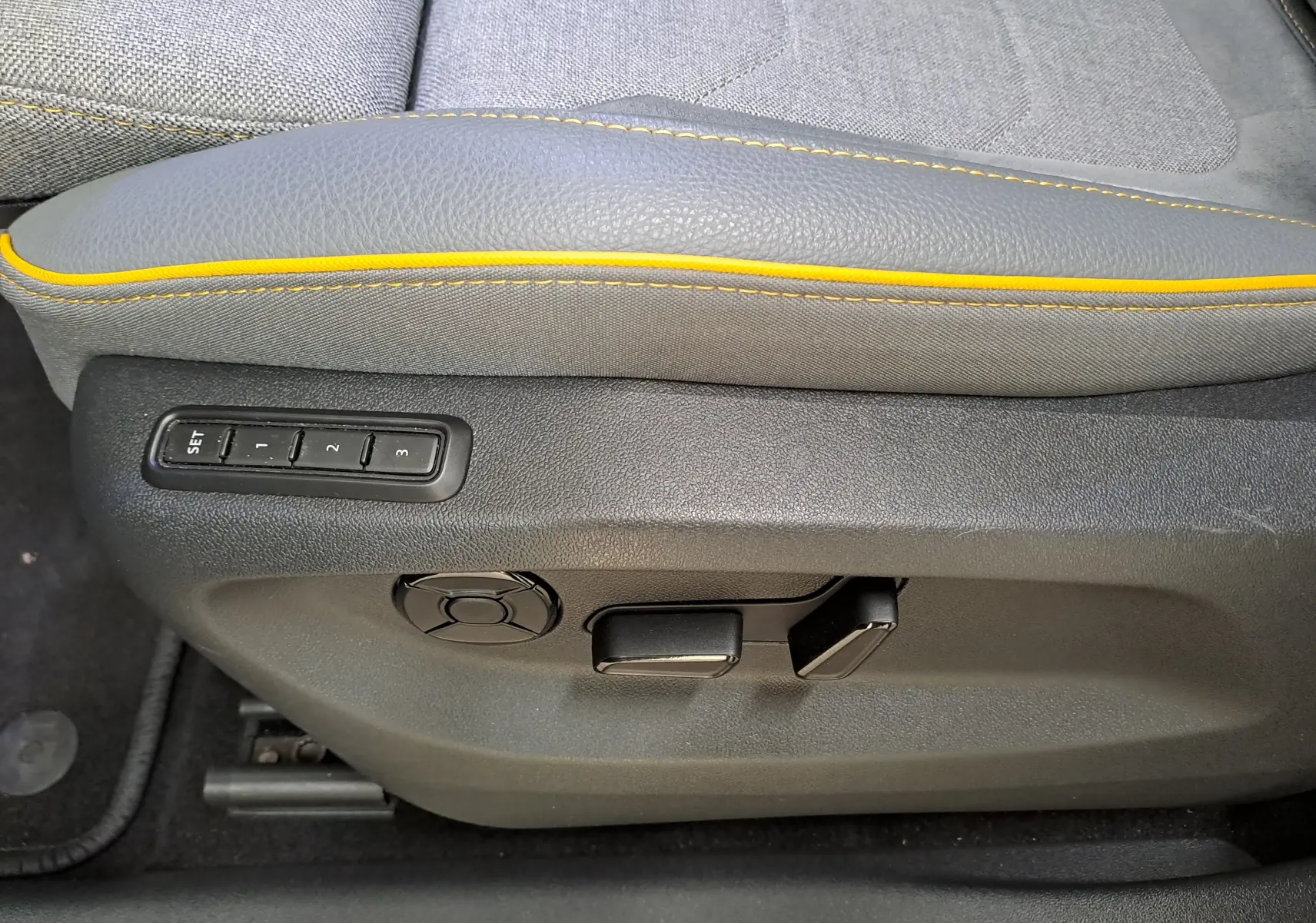 Réglages électriques et mémoire des positions sur le côté gauche d’un siège gris avec surpiqûres jaunes dans un Skoda Kodiaq hybride.