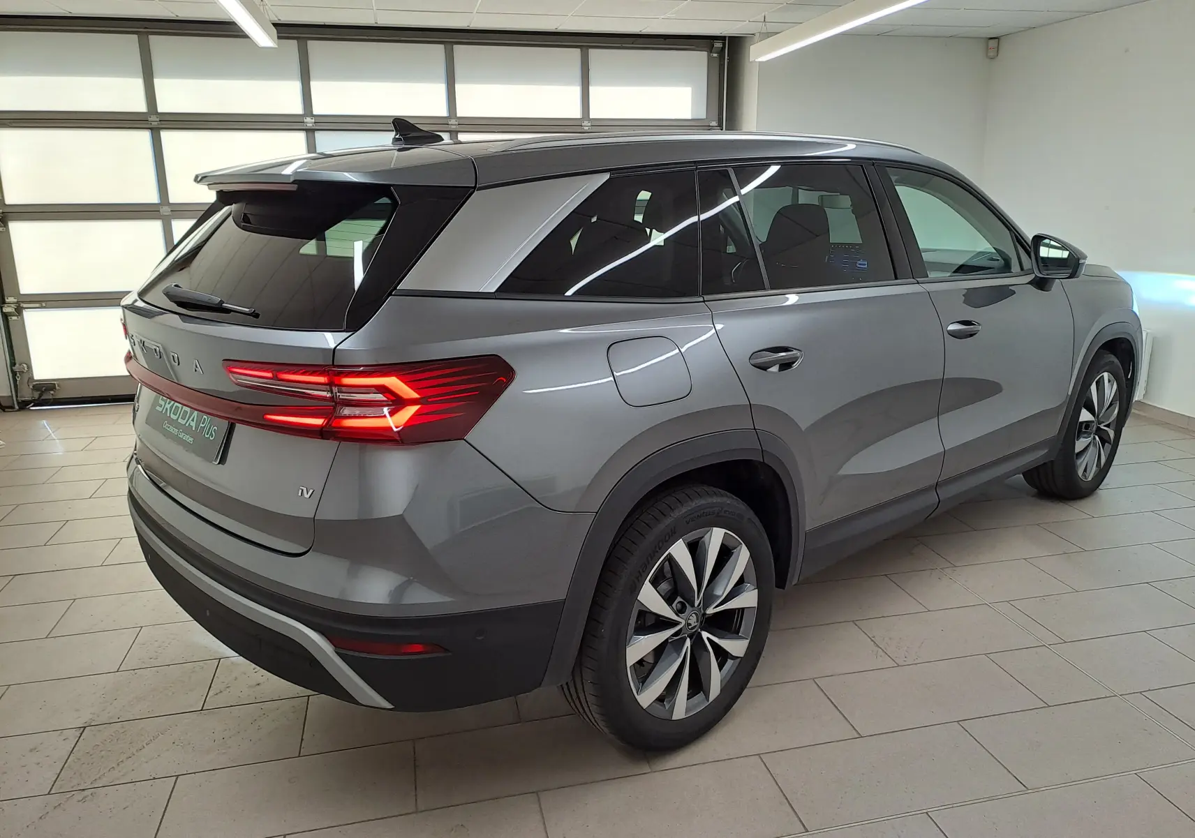 Vue 3/4 arrière droite d'un Skoda Kodiaq gris graphite hybride rechargeable avec feux arrière allumés en intérieur.