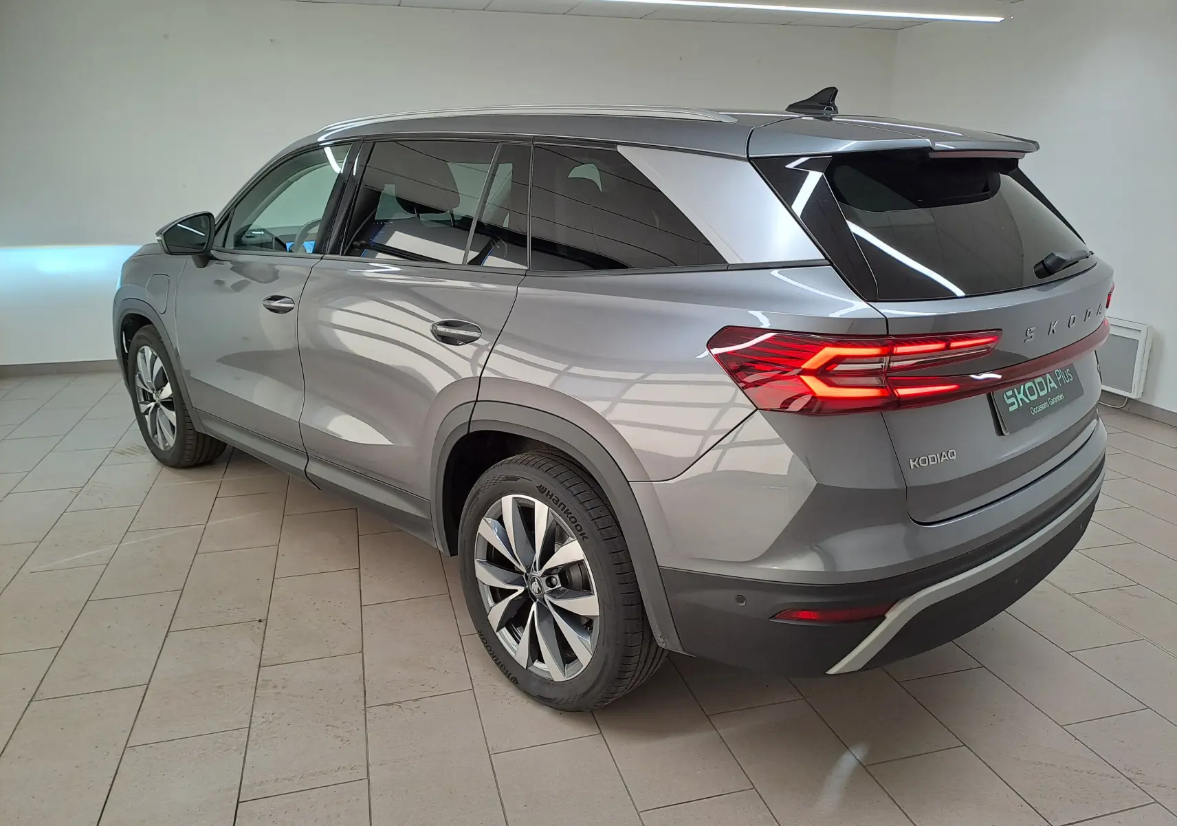 Vue 3/4 arrière droite du Skoda Kodiaq gris graphite 2025 avec feux arrière allumés et toit panoramique ouvrant.