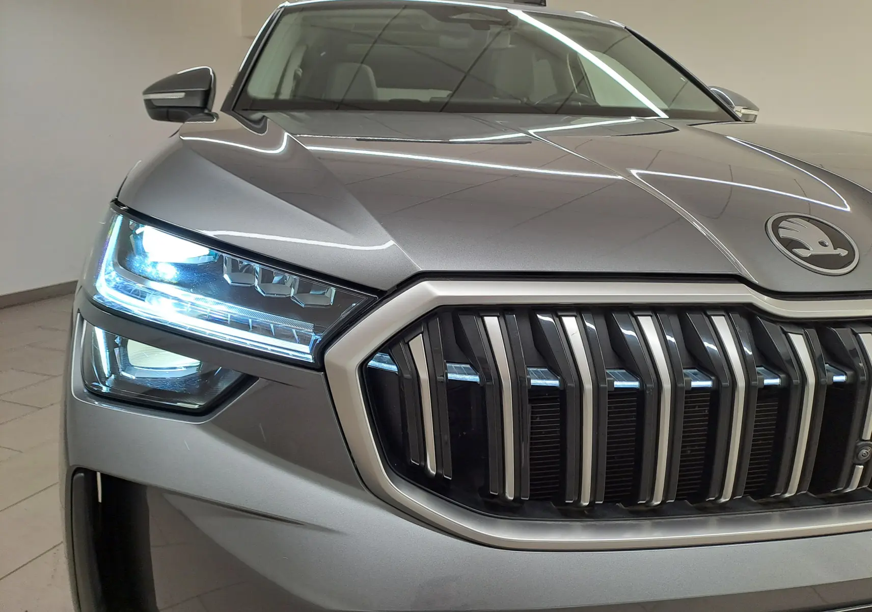 Gros plan avant gauche du Skoda Kodiaq gris graphite avec phares allumés et calandre verticale distinctive.