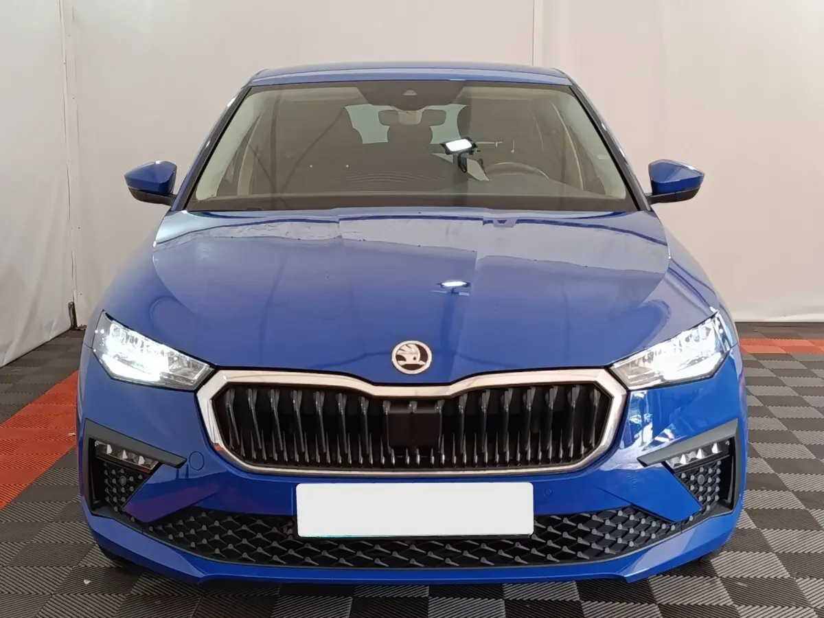 Vue avant d'une Skoda Scala bleu vif avec calandre noire et phares LED allumés dans un intérieur neutre.
