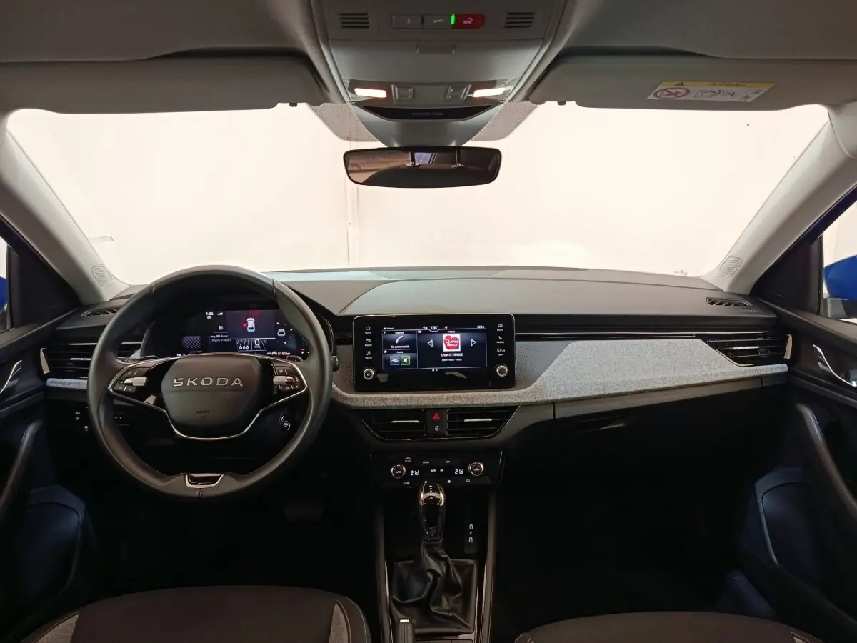 Vue intérieure avant du tableau de bord gris clair et noir du Skoda Scala bleu avec écran tactile central et volant multifonctions.