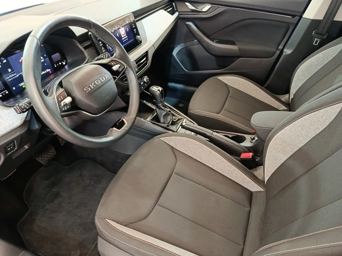 Vue intérieure côté conducteur de la Skoda Scala 2025, volant cuir, sièges tissu bicolore gris et noir, console centrale avec boîte manuelle.