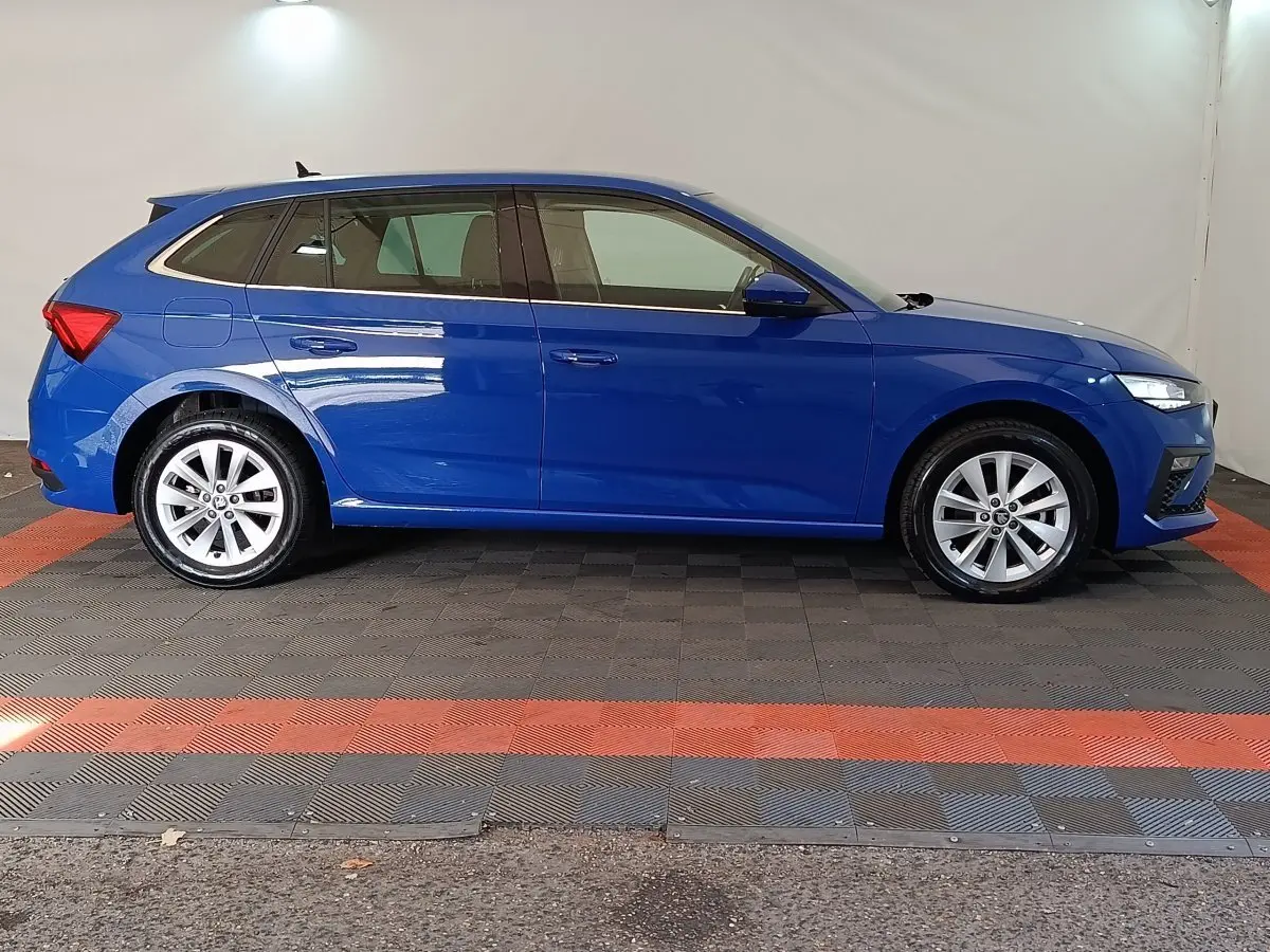 Vue latérale droite d'une Skoda Scala bleu 2025 avec jantes alliage et phares LED allumés dans un studio.