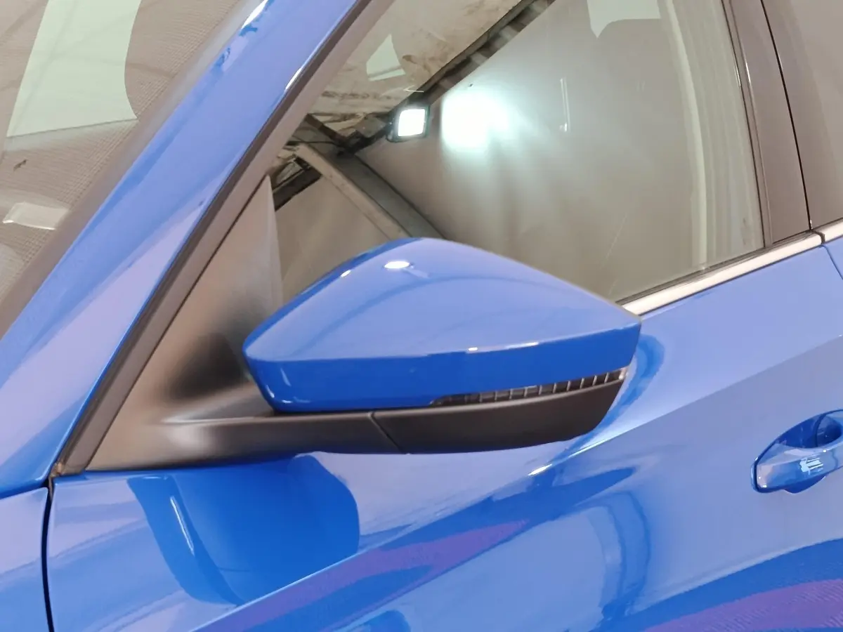 Gros plan sur le rétroviseur côté gauche bleu vif d'une Skoda Scala 2025 avec poignée de porte assortie.