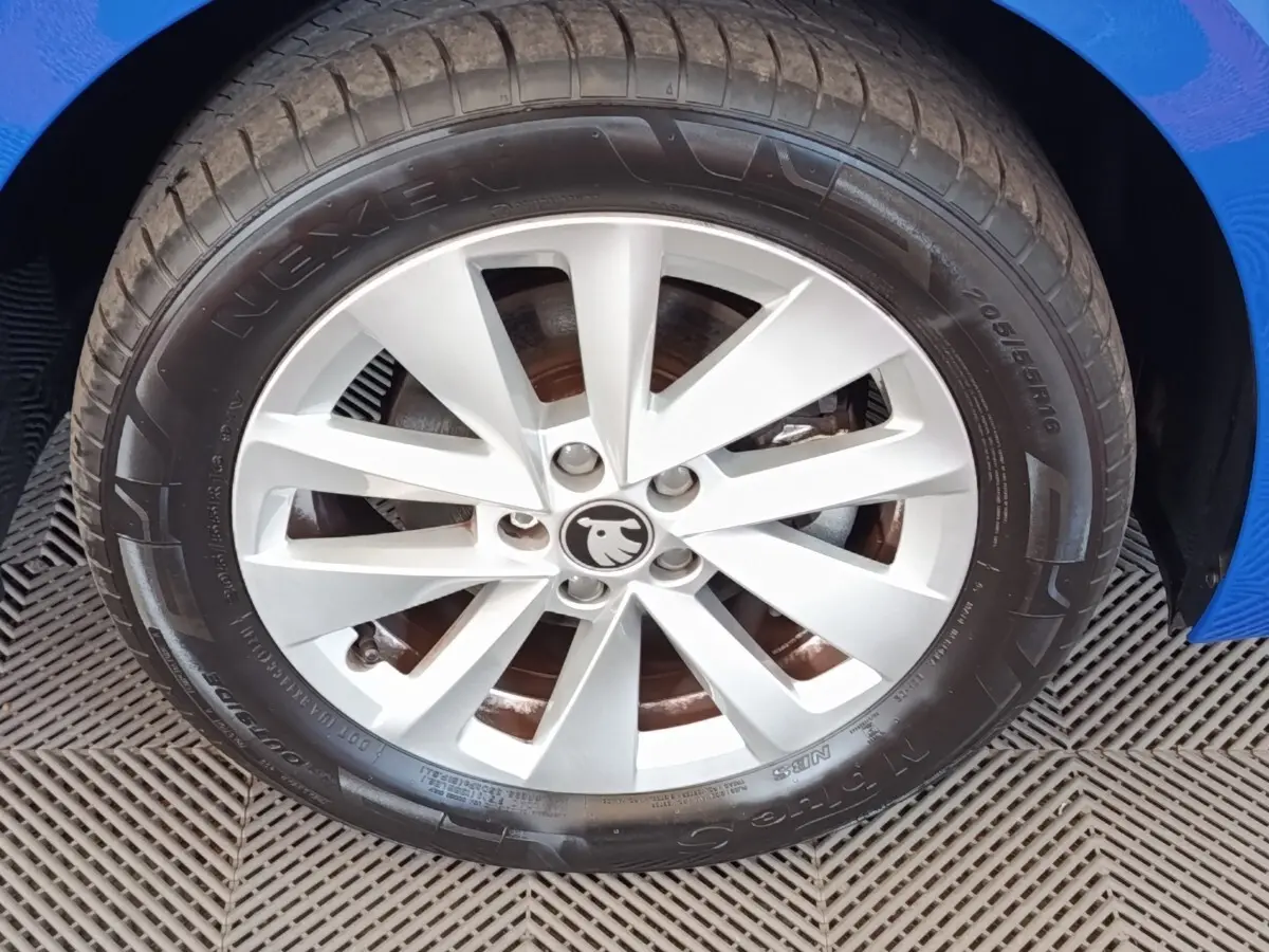 Gros plan sur la roue avant droite d'une Skoda Scala bleue, jante alliage argentée avec logo Skoda au centre.