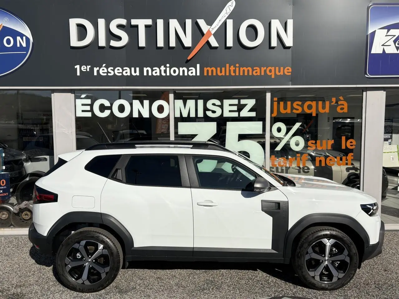 Profil droit du Dacia Duster 1.6 Hybrid blanc métallisé avec barres de toit noires et jantes alliage 18 pouces.
