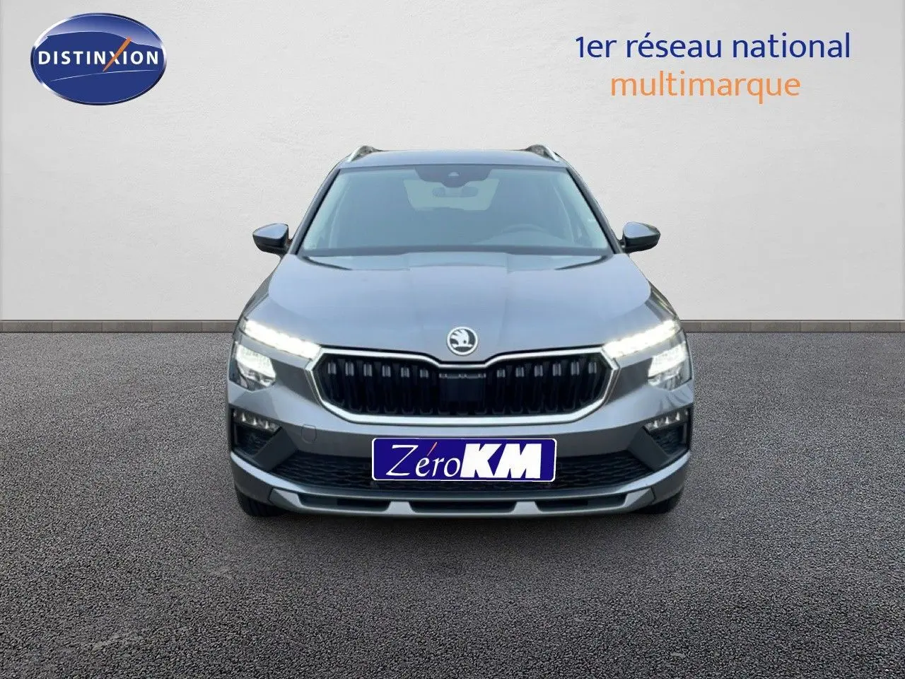 Vue frontale d'un Skoda Kamiq gris graphite métallisé avec phares LED allumés sur fond neutre.