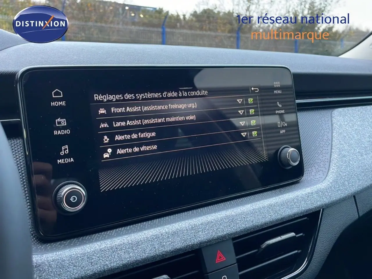 Vue intérieure centrée sur l'écran tactile du tableau de bord du Skoda Kamiq gris graphite, affichant les aides à la conduite.