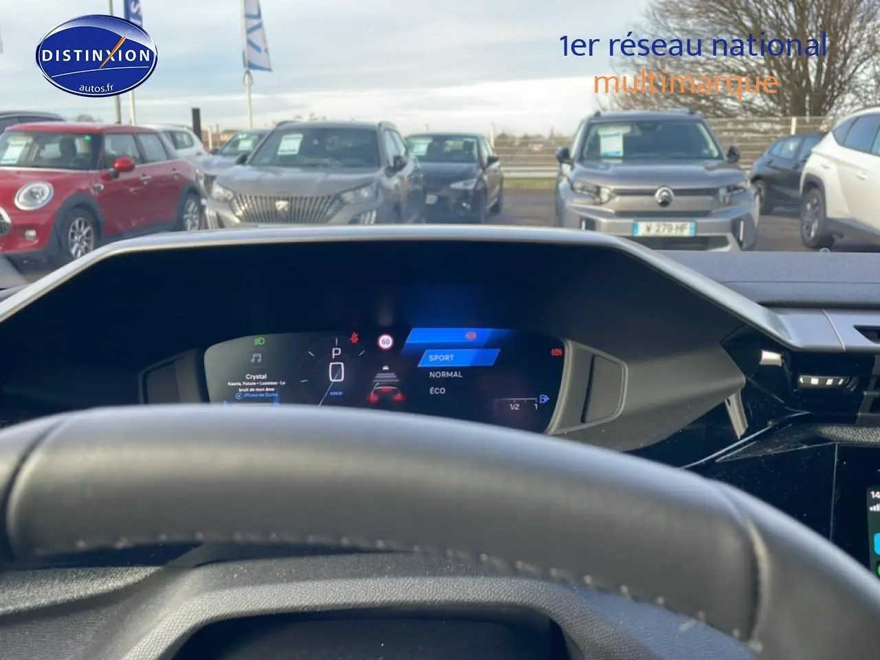 Vue depuis l'intérieur sur le tableau de bord numérique et le volant d'une Peugeot 308 gris artense, avec affichage mode de conduite.