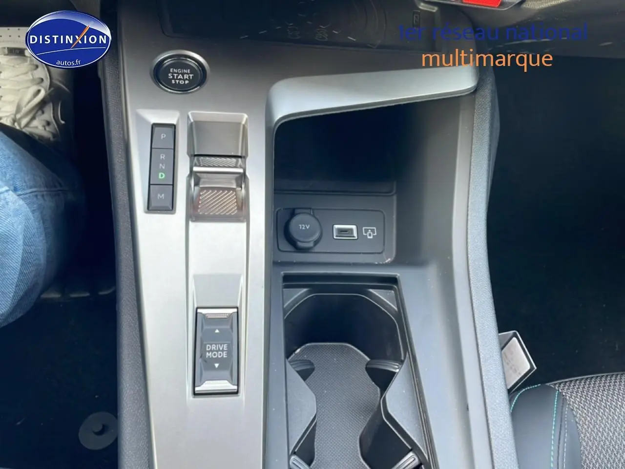 Vue plongeante sur la console centrale grise de la Peugeot 308 hybride 2025 avec bouton start et prise 12V visible.