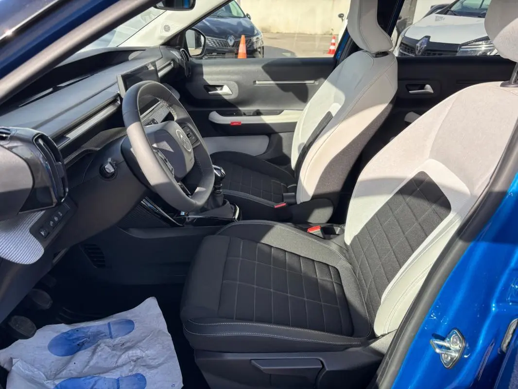 Vue intérieure côté conducteur de la Citroën C3 bleu 2025, sièges bicolores noir et gris, volant et tableau de bord visibles.