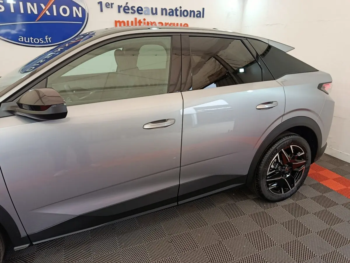 Profil droit du Peugeot 3008 gris clair hybride 2025 avec jantes noires et vitres teintées dans un showroom.