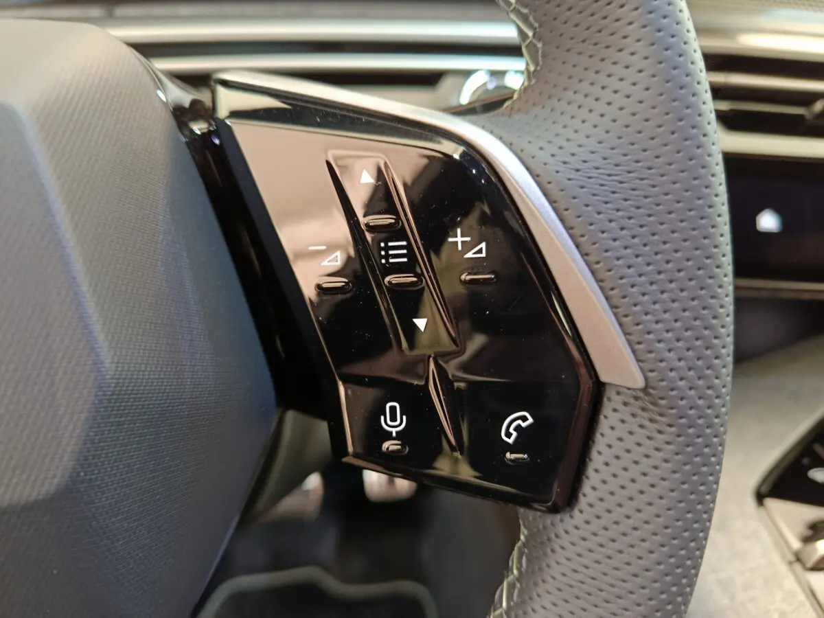 Gros plan sur les commandes tactiles noires du volant cuir perforé du Peugeot 3008 gris clair, version hybride 2025.