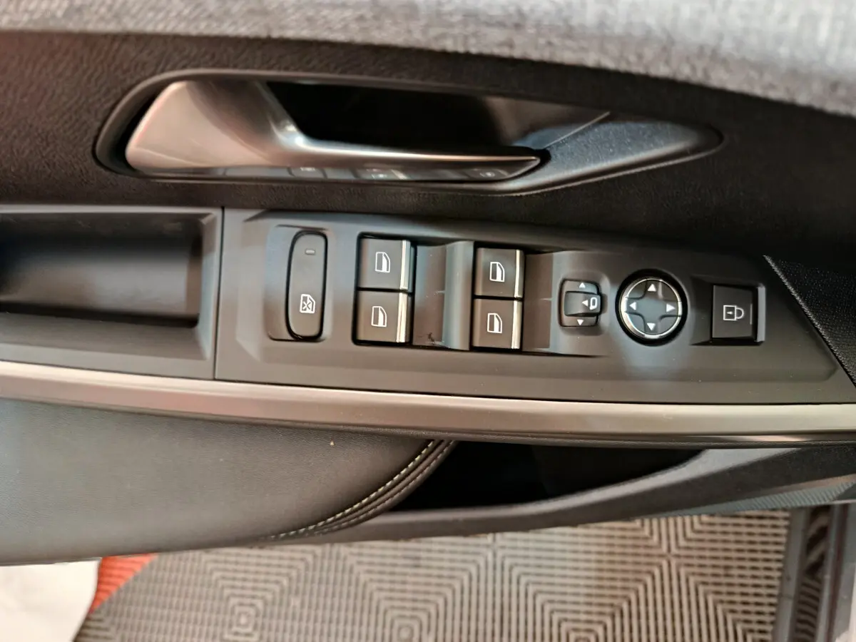 Gros plan sur la commande des vitres et rétroviseurs côté conducteur du Peugeot 3008 gris clair, intérieur cuir noir.