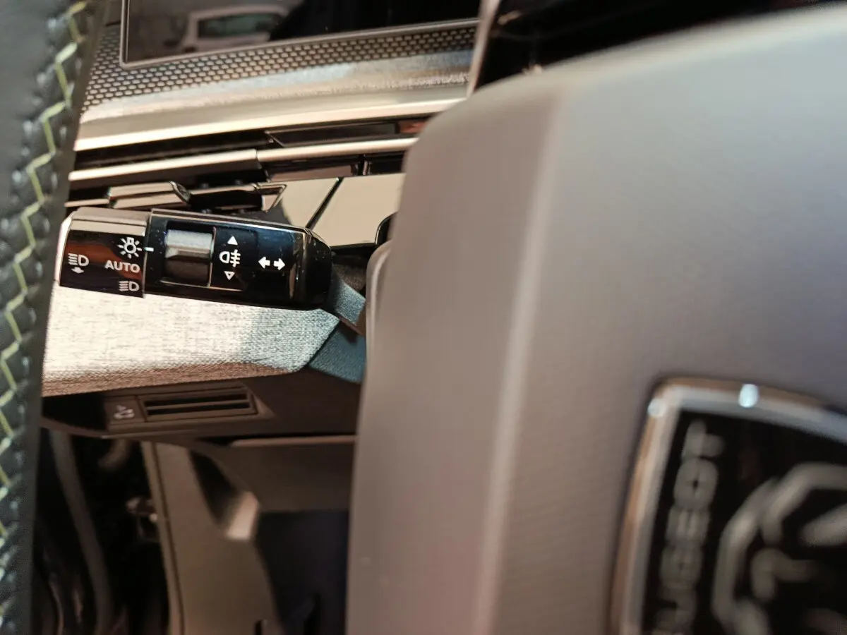 Détail intérieur du Peugeot 3008 gris clair, montrant la commande des feux sur la gauche du volant.